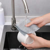A hand is using a faucet to pour water onto a mesh microfiber cloth placed in a white container for cleaning.