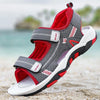 A pair of gray and red breathable summer sport sandals with adjustable straps resting on a sandy beach.