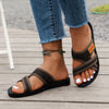 A pair of brown breathable mesh flat sandals with a cushioned sole worn by a person on a wooden deck.