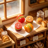 Et sett med miniatyrbakverk av resin, med en rød tomat og en oransje muffins, på en treoverflate.