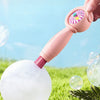A hand is using a pink foam wand to create a large bubble on green grass.