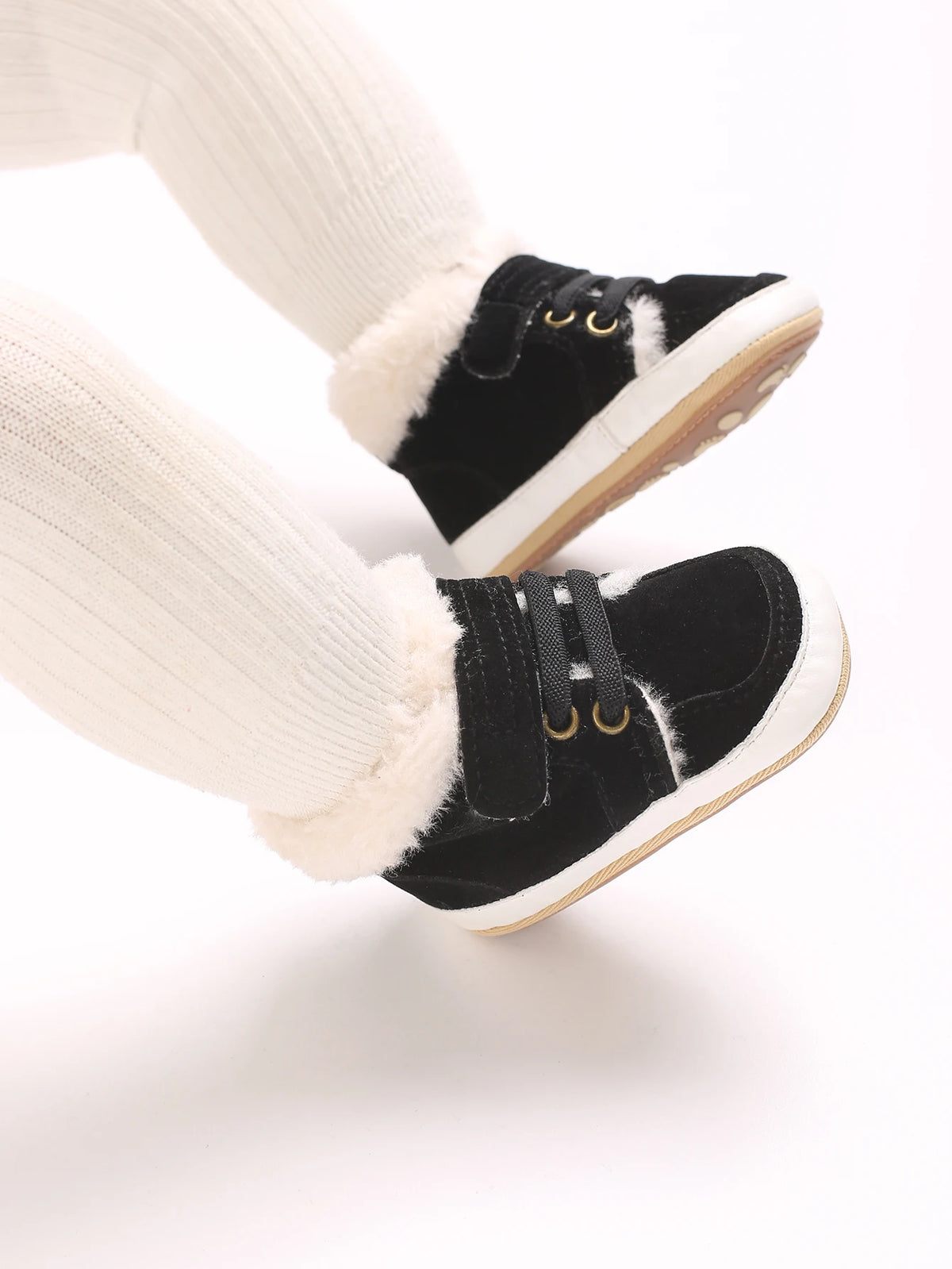 A pair of black baby winter snow boots with white fuzzy trim and light brown soles, shown on a leg.