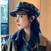 A woman wearing a black PU leather beret hat and a dark jacket looking to the side.