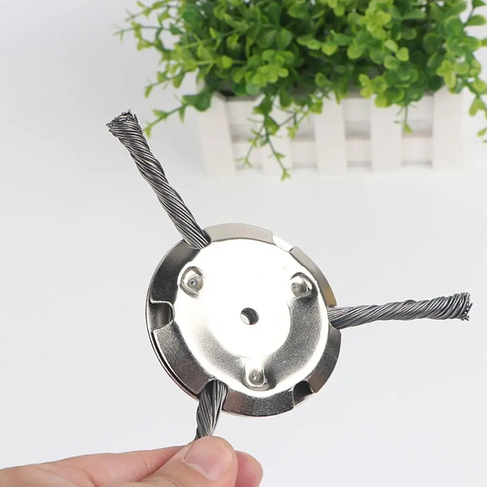 A close-up of a steel wire brush trimmer head with a cutting wire and mounting plate being held by a hand.