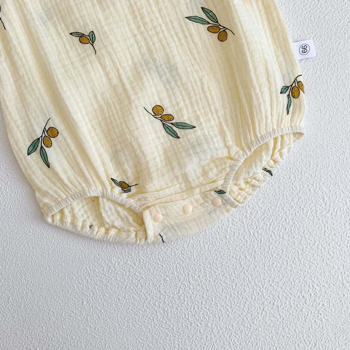 A cream-colored baby cotton sleeveless jumpsuit bodysuit set with small olive leaf embroidery.