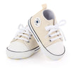 A pair of beige canvas baby sneakers with white laces and a soft non-slip sole.
