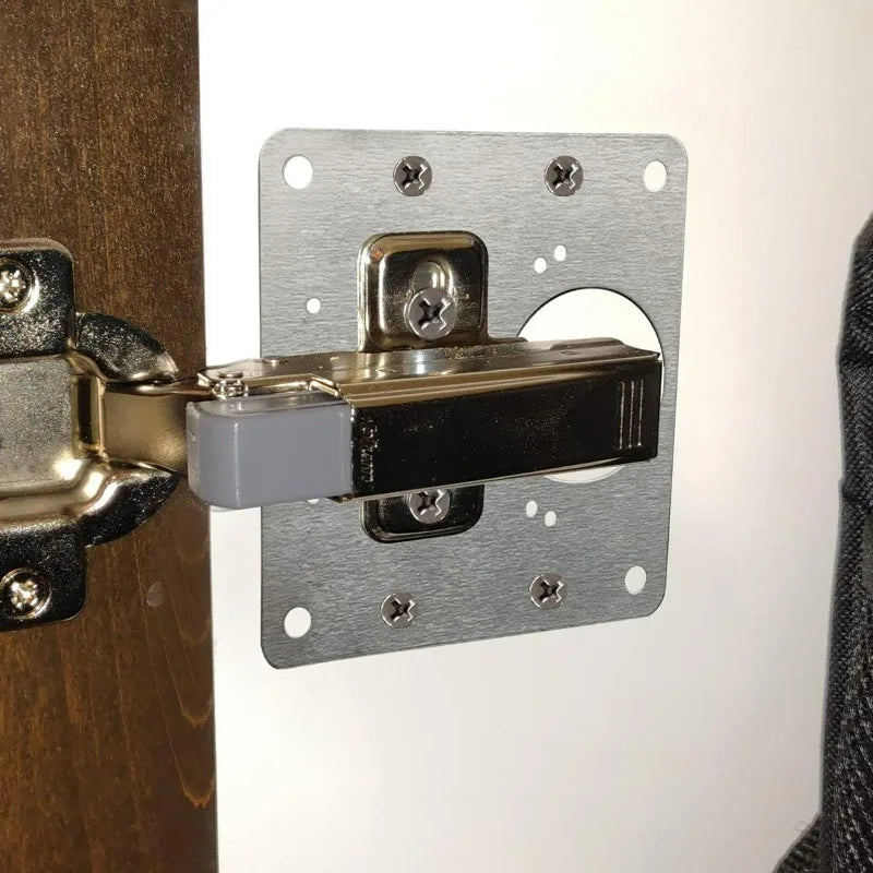 Stainless steel cabinet door hinge repair plate kit with screws mounted on a wooden surface.