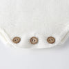 Close-up of a white knitted baby romper featuring three small brown buttons on the chest area.
