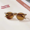 A pair of light brown sunglasses resting on a white surface next to a piece of paper.