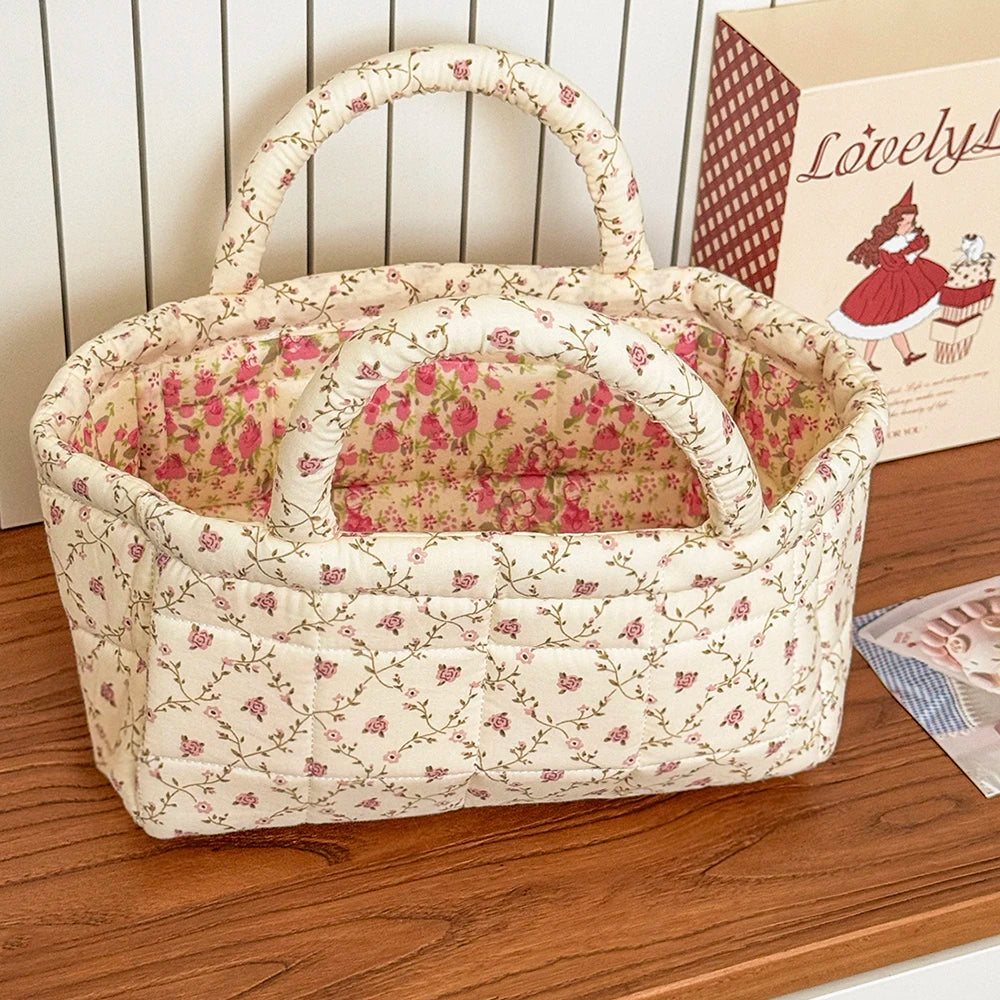 Kurv i kremfarget quilting med rosa blomstermønster og håndtak, stående på treoverflate.