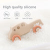 A beige silicone teether toy car with rounded parts is shown nestled in white granular material.