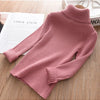 A pink ribbed knit turtleneck sweater laid flat on a wooden surface next to a book.