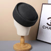 Black straw pillbox sun hat displayed on a wooden mannequin against a light background.