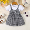 A black and white plaid girls' cotton knit dress with a bow detail displayed on a hanger.