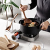 A person is using a natural teak wood cooking utensil, such as a spoon or spatula, in a black non-stick pan on an electric co