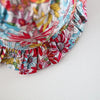 A close-up of a baby girl's floral print dress with ruffled trim and matching hat.