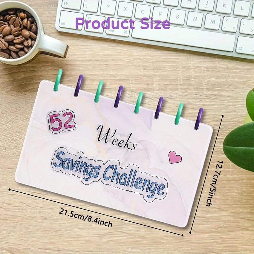A pink marble-patterned planner or binder titled 52 Weeks Savings Challenge lying on a wooden surface next to a laptop keyboa