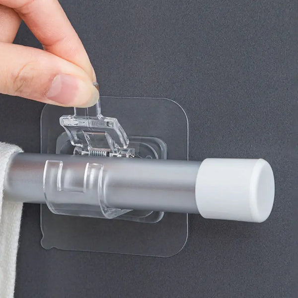 A hand is clipping a clear plastic hook onto a silver curtain rod using self-adhesive clips.
