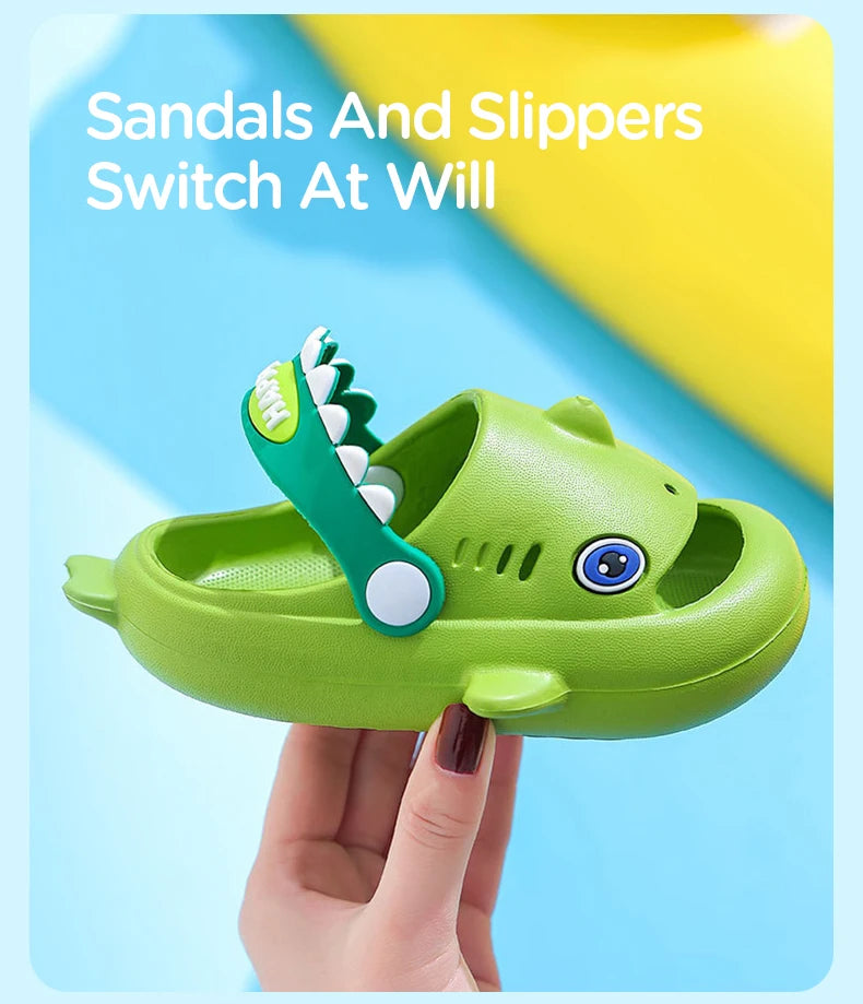 A hand holds a green kids shark clog sandal, demonstrating the switch at will feature.