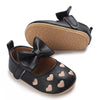A pair of black baby first walker shoes with a bow and heart pattern on the toe