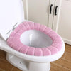 A pink soft acrylic toilet seat cover is placed on a white toilet bowl.