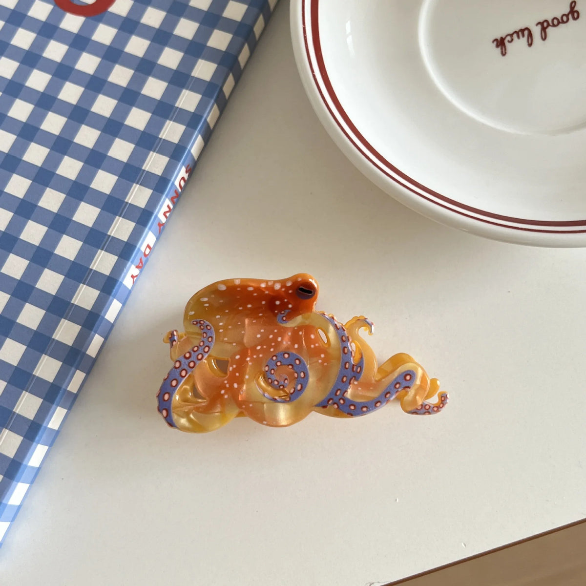 En vevd hårklemme med blekksprut- og haidesign i gjennomsiktige oransje og blå toner.