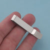 A silver metal tie clip is held between fingers against a light blue background.