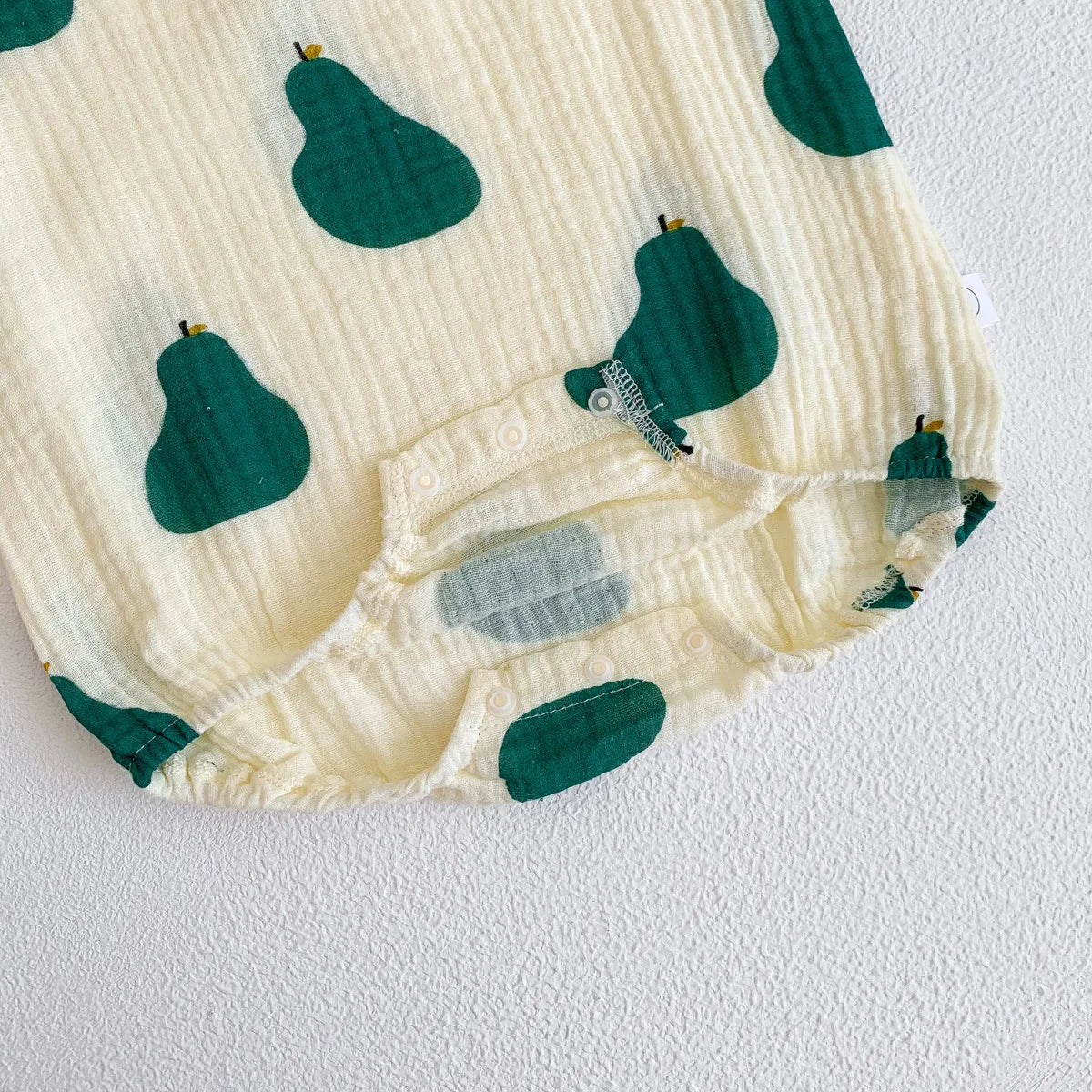 A cream-colored baby cotton sleeveless jumpsuit bodysuit set with a green pear print.