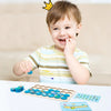 A toddler is playing a wooden memory chess game with colorful tiles on a white surface.