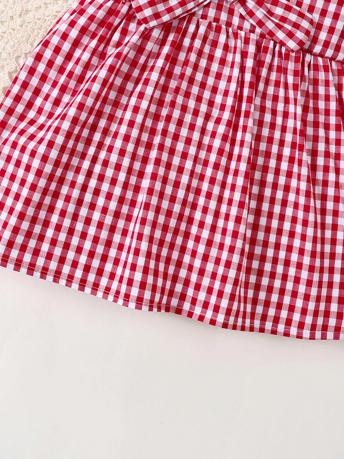 A close-up of a red and white gingham cotton knit dress with a bow accent.