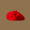 A bright red classic wool beret hat viewed from above against a neutral brown background.