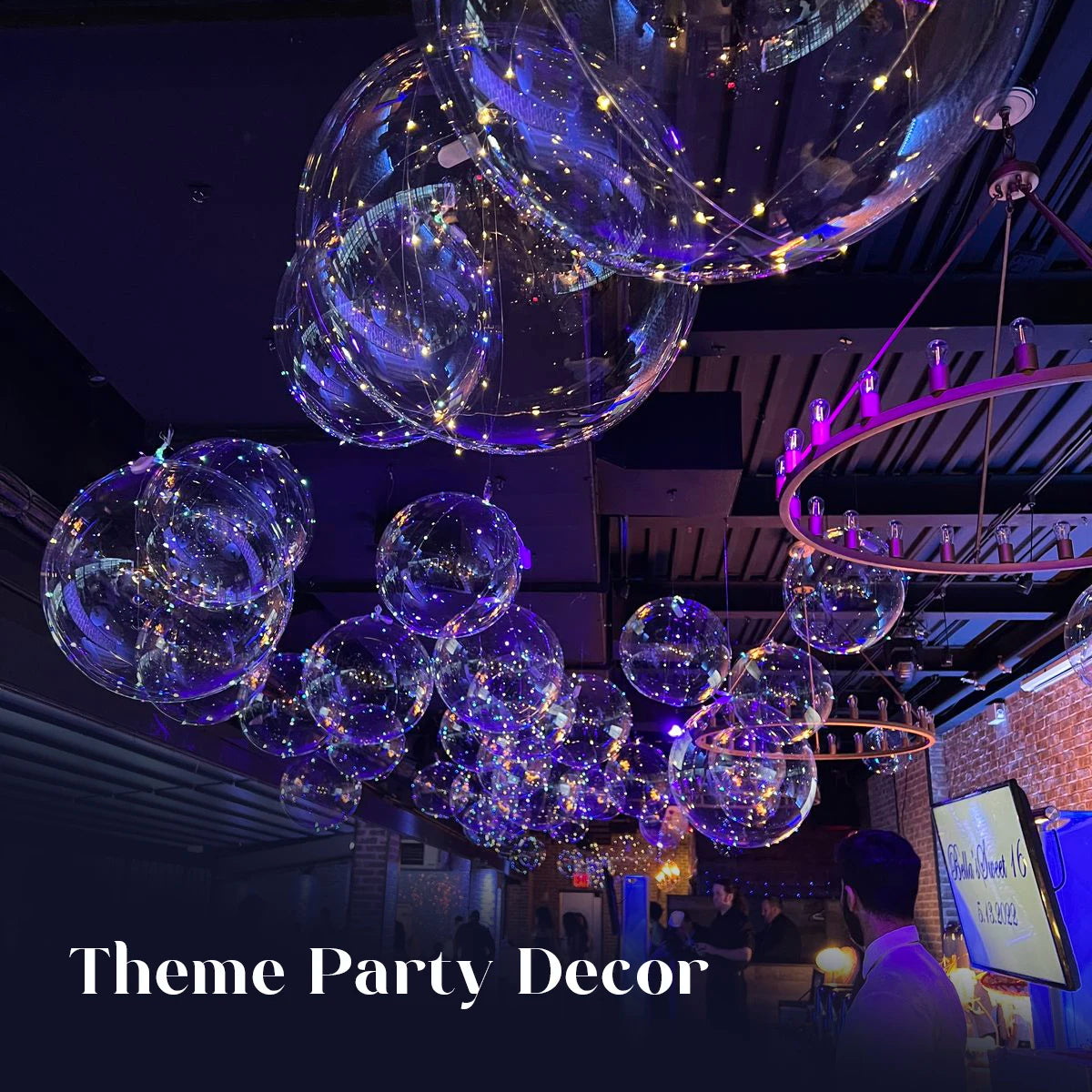 A cluster of glowing purple and blue LED light-up balloons suspended from the ceiling in a dark venue.