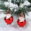 A set of two shiny red Christmas tree ornaments with white Santa faces hanging on a green pine branch.