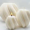 Three white pillar candles with a wavy texture and a flame on a light surface.