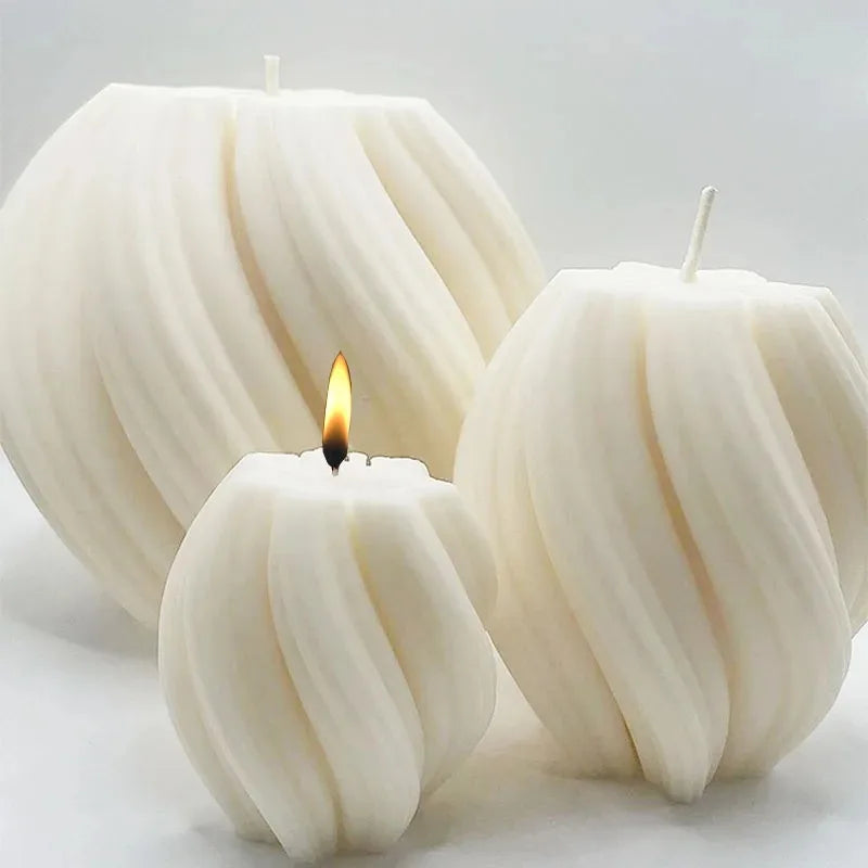 Three white pillar candles with a wavy texture and a flame on a light surface.