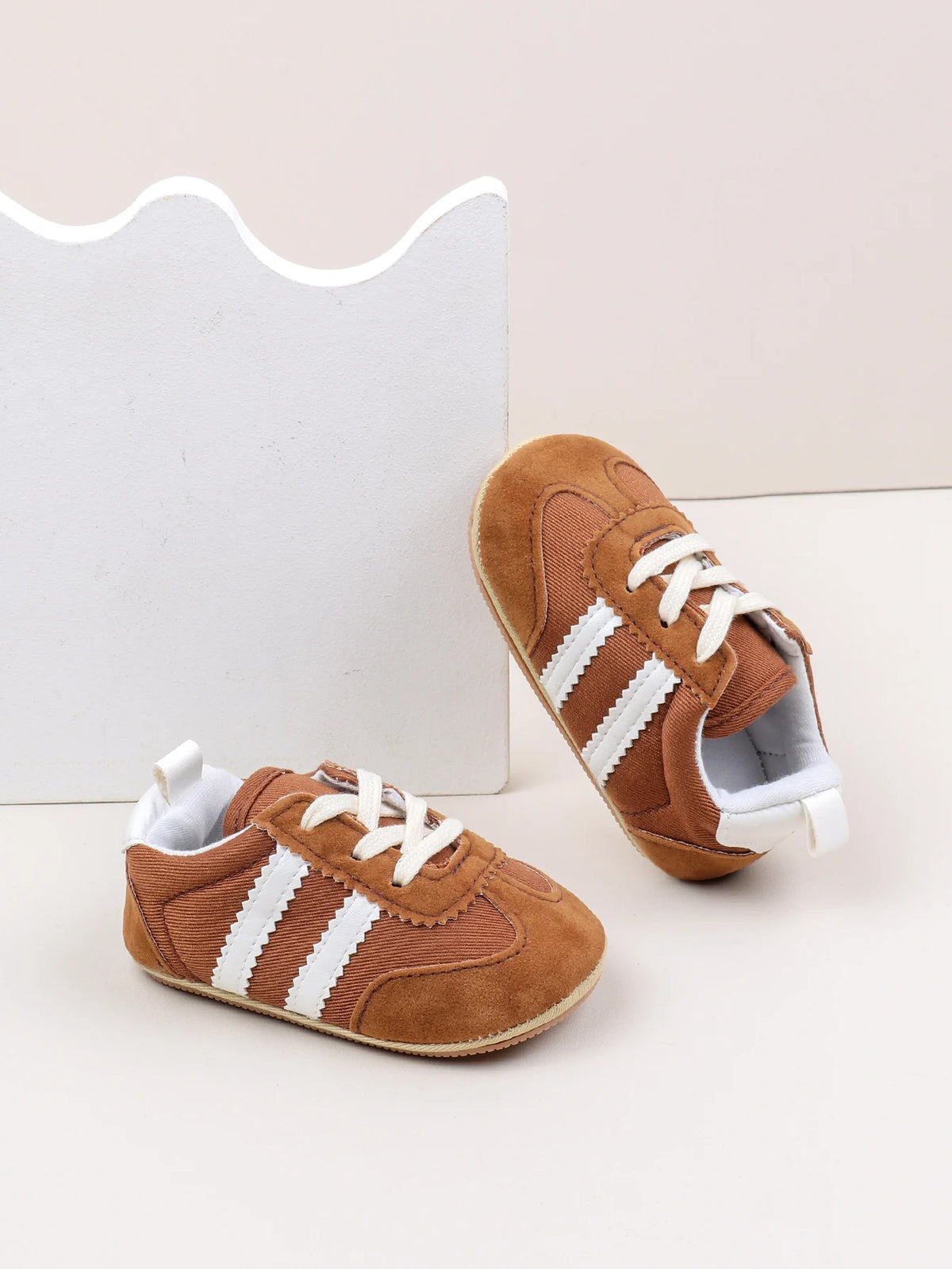 A pair of brown baby first walker shoes with white stripes and a light gray sole are shown against a white background.