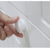A hand is opening a white cabinet door, showing a magnetic safety lock mechanism.