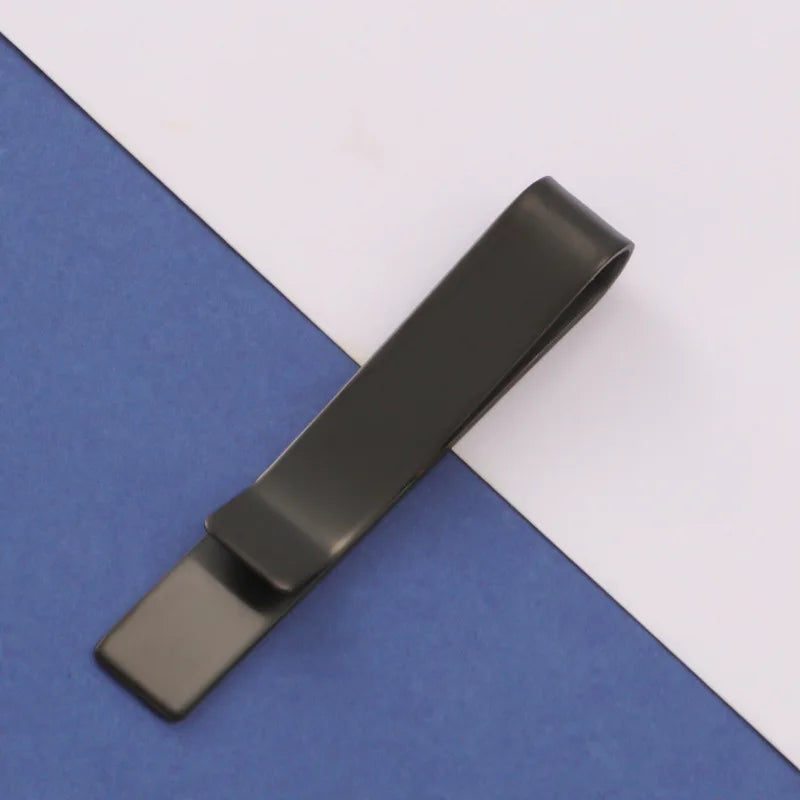 A dark metal tie clip lying diagonally on a blue-gray fabric surface.