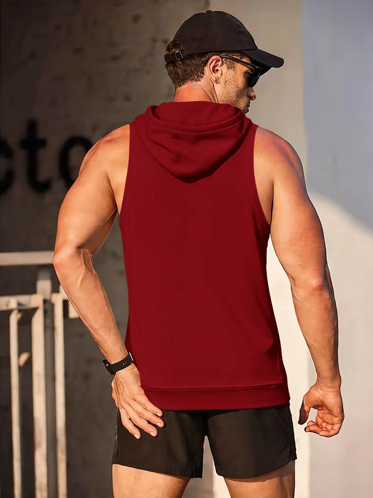 A muscular man wearing a maroon performance hooded tank top and black shorts, viewed from the back.