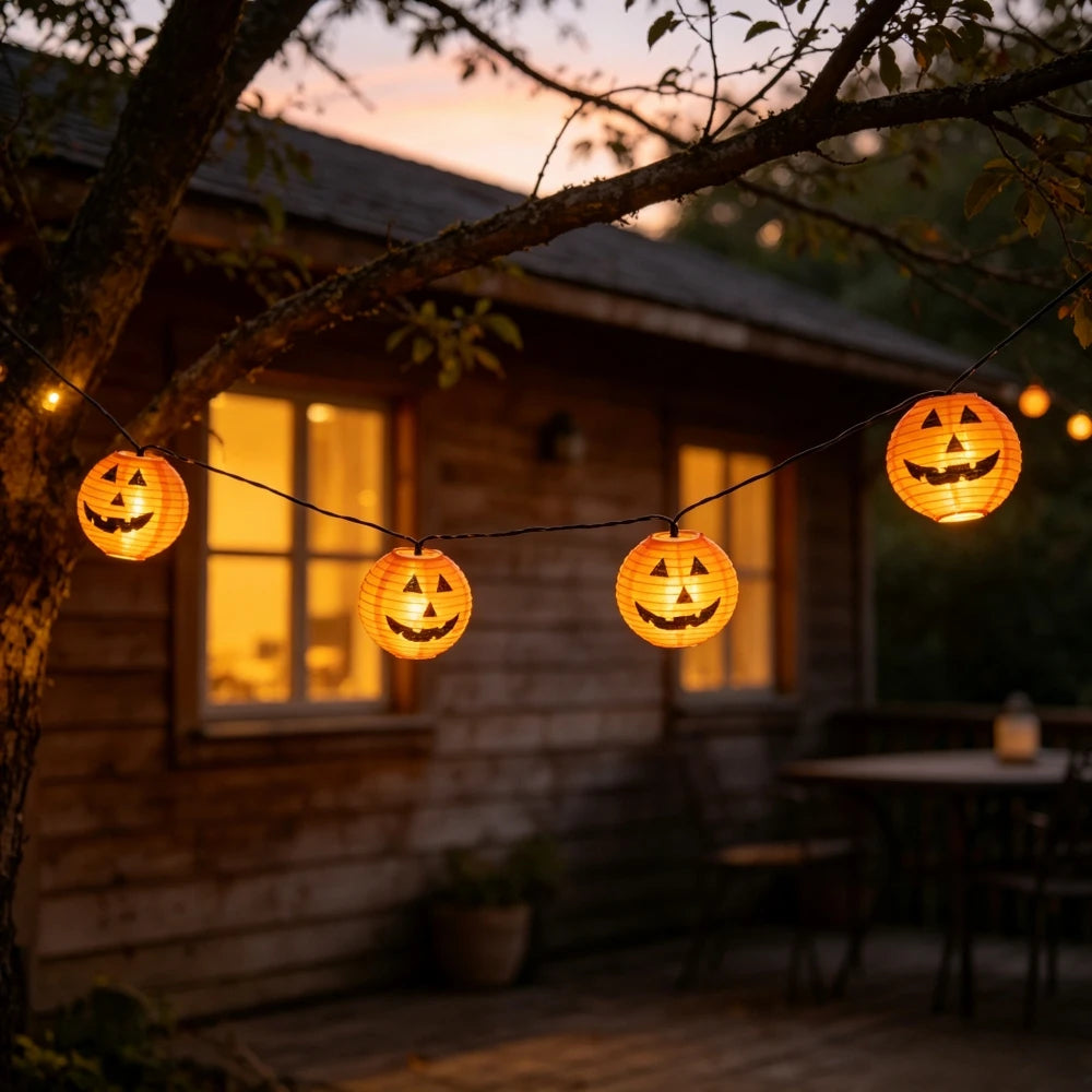 String lights featuring carved pumpkin lanterns hanging in front of a wooden house at sunset