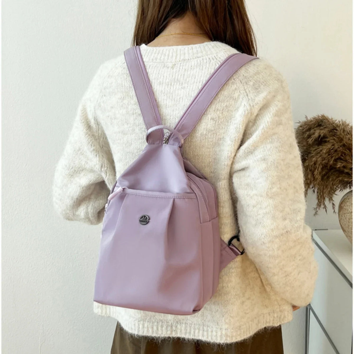 A woman is wearing a light pink mini backpack over a cream knit sweater.