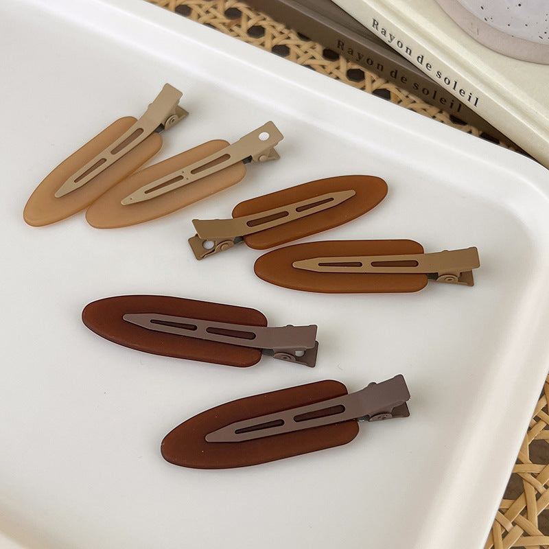 A set of two matte resin side hair clips in various shades of brown and tan are displayed on a white tray.