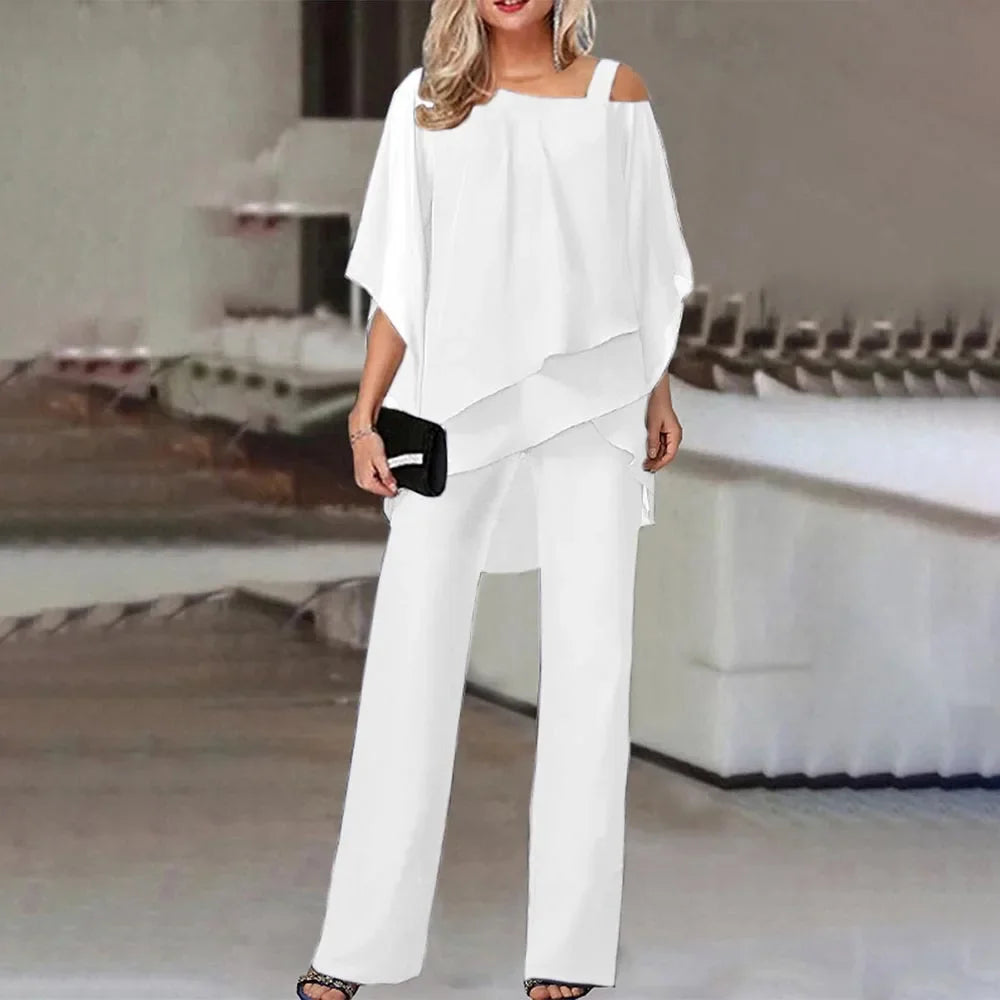En kvinne modellerer et hvitt todelt sett med en off-shoulder topp og vide bukser.