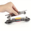 A hand holds a stainless steel double-headed measuring spoon set with magnetic storage, showing various sized spoons in diffe