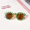 Green and white checkered sunglasses with amber lenses resting on a white background.
