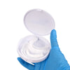 A hand in a blue glove holds an open white cosmetic denture teeth kit container.