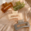 Three matte finish jelly hair claw clips in amber, lime green, and gray are displayed on a sheer fabric.