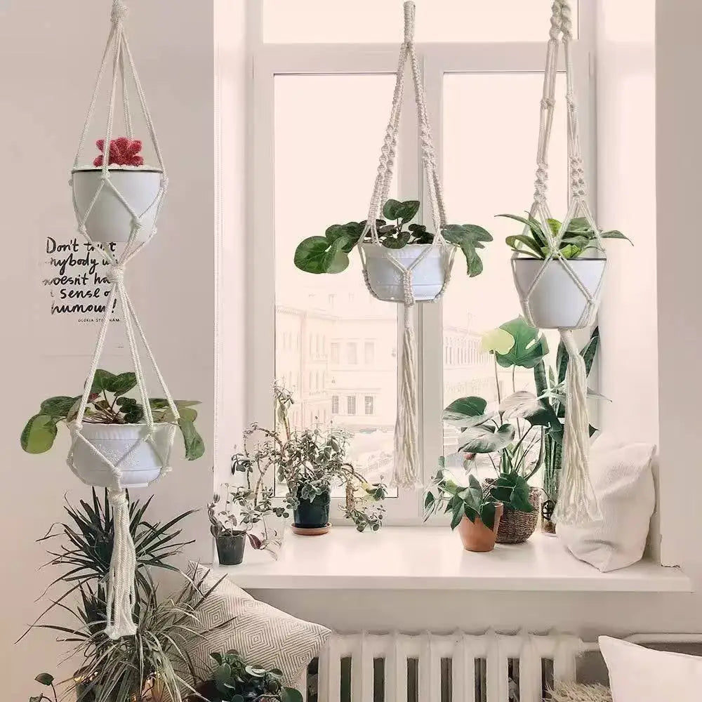 En samling håndlagde macrame-plantekasser med grønne planter og hvite potter i vinduskarmen.