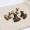Et sett med vintage messingfrosk-miniatyrfigurer som hviler på en beige stoffoverflate.