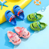 A collection of colorful kids shark clog sandals in blue, green, and pink resting on a light blue surface.
